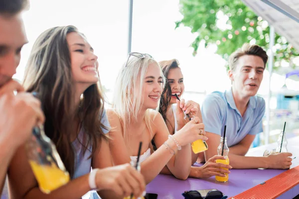 Una compañía de amigos guapos riéndose, bebiendo cócteles amarillos y socializando en el bar en el agradable café de verano. El río está al fondo. ¡Salud! Entretenimiento, pasar un buen rato — Foto de Stock