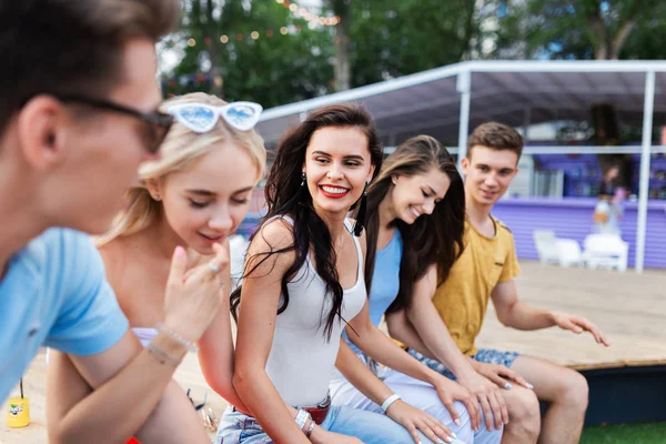 A company of good-looking friends laughing and socialising while sitting on the bench in the nice summer cafe. Cheers. Entertainment, having good time. Friendship.