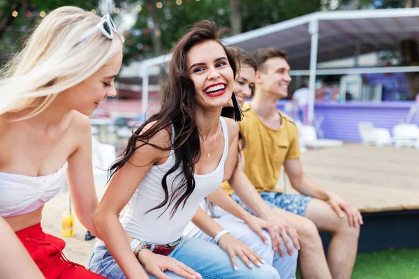 A company of good-looking friends laughing and socialising while sitting on the bench in the nice summer cafe. Cheers. Entertainment, having good time. Friendship.