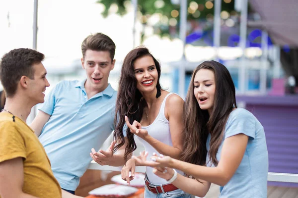 Eine Gruppe gut aussehender Freunde sitzt lachend am Geländer des netten Sommercafés. Unterhaltung, Spaß haben. Freundschaft. — Stockfoto