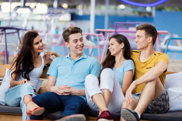 Eine Gruppe gut aussehender Freunde sitzt lachend auf der Bank mit Kissen im netten Sommercafé. Unterhaltung, Spaß haben. Freundschaft. — Stockfoto
