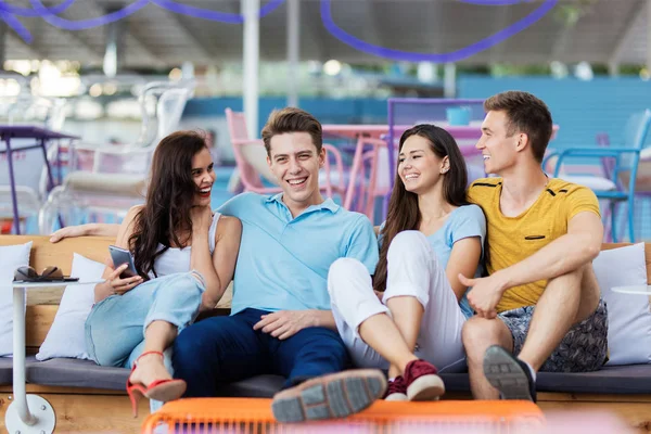 Eine Gruppe gut aussehender Freunde sitzt lachend auf der Bank mit Kissen im netten Sommercafé. Unterhaltung, Spaß haben. Freundschaft. — Stockfoto