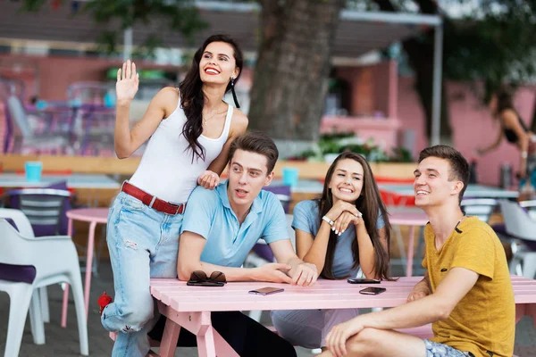 A company of good-looking friends is laughing, socialising and sitting at the table in the nice summer cafe. Entertainment, having good time. Friendship.