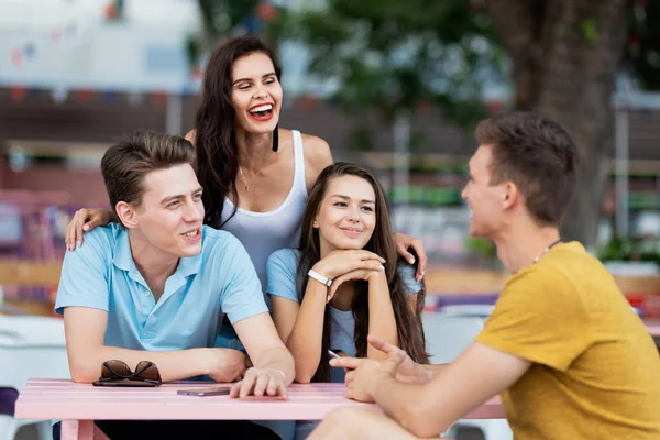 A company of good-looking friends is laughing, socialising and sitting at the table in the nice summer cafe. Entertainment, having good time. Friendship.