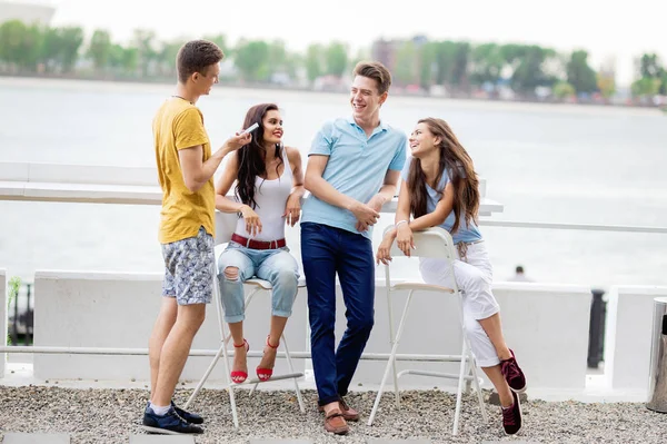 Uma companhia de amigos bonitos está rindo e socializando no agradável café de verão. O rio está no fundo. Entretenimento, divertindo-se. Amizade . — Fotografia de Stock