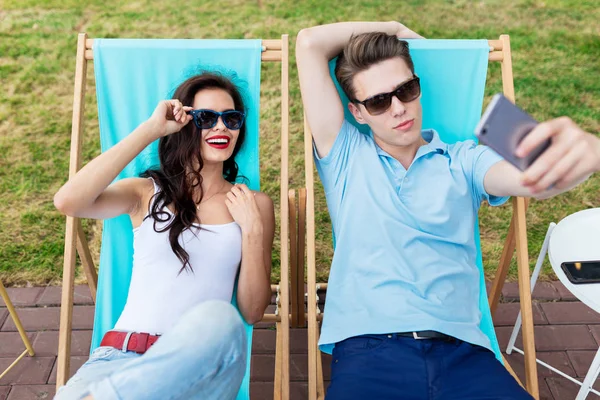 Ein schönes Paar mit Sonnenbrille liegt auf den Liegestühlen auf der Liegewiese im netten Sommercafé. Unterhaltung, Spaß haben. Freundschaft, Beziehung. — Stockfoto