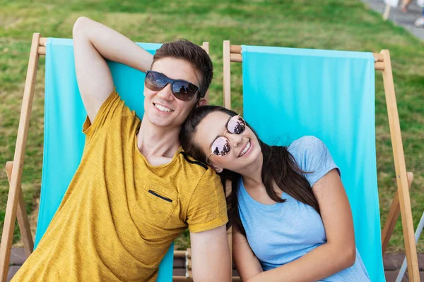 A beautiful couple in the sunglasses is lying on the deck chairs on the lawn in the nice summer cafe. Entertainment, having good time. Friendship, relationship. — Stock Photo, Image