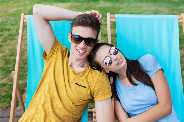 Ein schönes Paar mit Sonnenbrille liegt auf den Liegestühlen auf der Liegewiese im netten Sommercafé. Unterhaltung, Spaß haben. Freundschaft, Beziehung. — Stockfoto