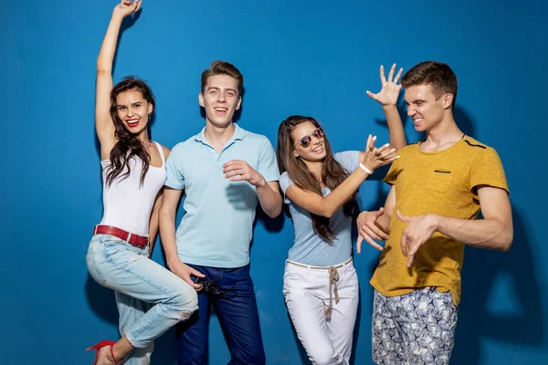 Quattro amici di bell'aspetto ridono mentre stanno in piedi davanti al muro blu con sguardi sicuri e felici. Intrattenimento, divertirsi. Amicizia, relazione . — Foto Stock