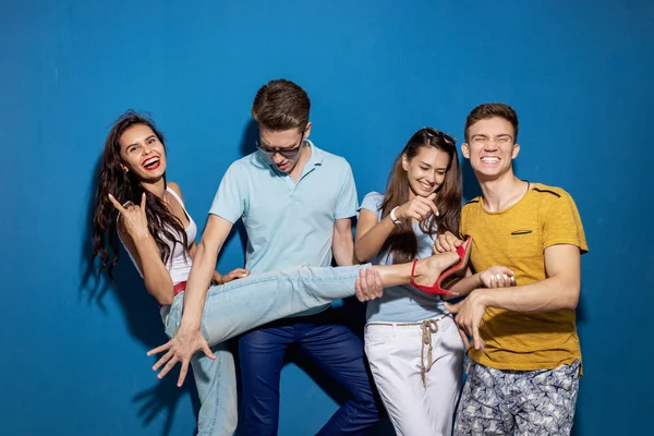 Cuatro amigos guapos se ríen mientras están de pie frente a la pared azul con miradas confiadas y felices. Entretenimiento, pasándolo bien. Amistad, relación . — Foto de Stock