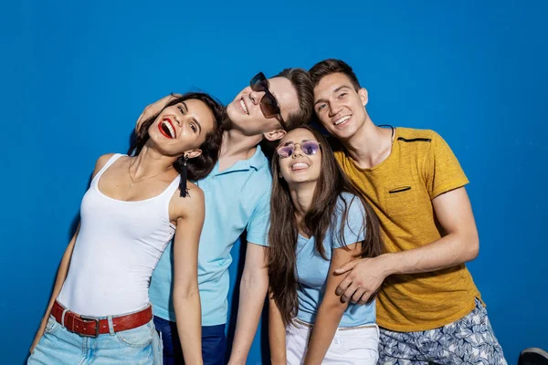 Cuatro amigos guapos se ríen mientras están de pie frente a la pared azul con miradas confiadas y felices. Entretenimiento, pasándolo bien. Amistad, relación . — Foto de Stock