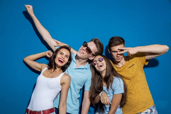 Τέσσερις όμορφος φίλοι γελούν ενώ στέκεται μπροστά από το μπλε τοίχο έχοντας μοιάζει σίγουρη και χαρούμενη. Ψυχαγωγία, έχοντας καλή στιγμή. Φιλία, σχέση. — Φωτογραφία Αρχείου