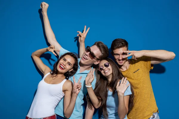 Vier gut aussehende Freunde lachen, während sie vor der blauen Wand stehen und selbstbewusst und glücklich aussehen. Unterhaltung, Spaß haben. Freundschaft, Beziehung. — Stockfoto