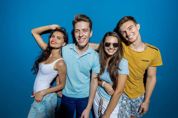 Quatro amigos bonitos estão rindo enquanto estão em frente à parede azul com looks confiantes e felizes. Entretenimento, divertindo-se. Amizade, relação . — Fotografia de Stock