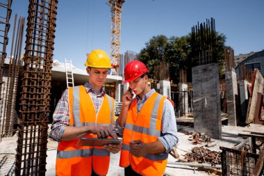 İnşaat mühendisi ve mimar turuncu iş yeleği giymiş ve zor şapka inşaat süreci telefonla görüşmek ve tablet açık şantiyeye kullanın