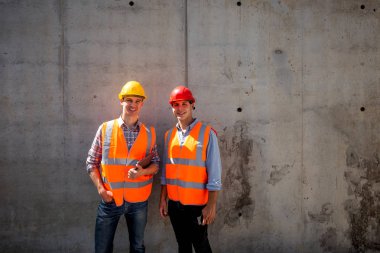 İnşaat mühendisi ve mimar turuncu iş yeleği giymiş ve kask bir beton duvar arka plan üzerinde durmak . .