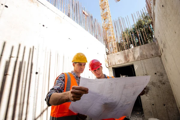 Bouw manager en ingenieur gekleed in werkkleding en veiligheidshelmen verkennen projectdocumentatie op de bouwplaats — Stockfoto