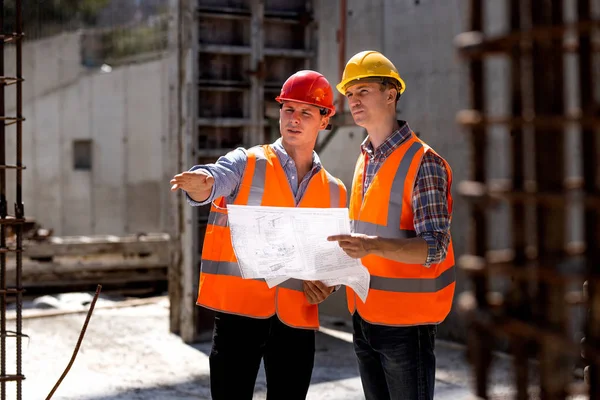 Väg-och vattenbyggnadsingenjör och byggledare i orange arbete västar och hårda hjälmar utforska konstruktion dokumentation på webbplatsen byggnad nära stålramar — Stockfoto