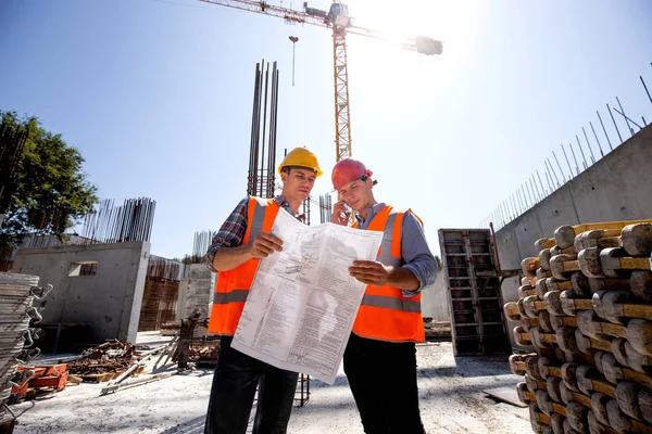 Strukturella ingenjör och konstruktion manager i orange arbete västar och hårda hjälmar diskutera dokumentation och prata via telefon på öppna luften byggnadsplatsen bredvid kranen — Stockfoto