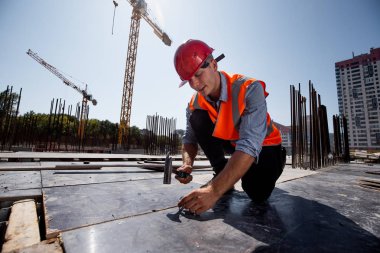 Turuncu iş yelek ve kask giymiş Oluşturucusu açık inşaat alanında bir çivi çekiç
