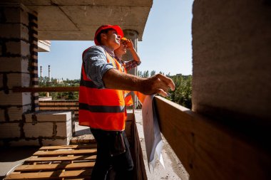 Turuncu iş yelek ve kask kürsüye şantiye inşaat altında binanın içinde giyinmiş iki genç İnşaat Mühendisleri