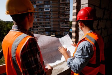 Mimar ve inşaat mühendisi gömlekler, turuncu iş yeleği giymiş ve kask binanın yapım aşamasında içinde bina sitede inşaat dokümantasyon keşfetmek