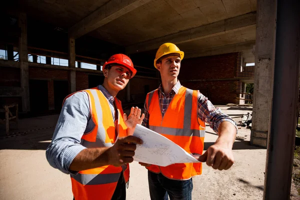 Architect  and structural engineer  dressed in orange work vests and helmets work documentation inside the building under construction