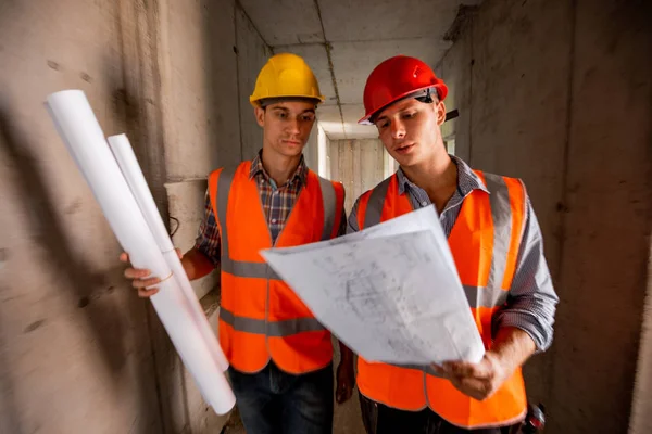Két férfi öltözött narancs munka mellény és sisak dolgozni építési dokumentációt belső rész a épület, építés alatt — Stock Fotó