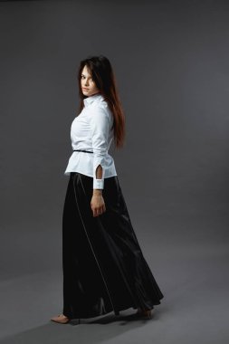 Stüdyoda koyu gri arka plan üzerinde siyah kuşak ve geniş siyah pantolon beyaz gömlek giymiş genç kadın güzel duruyor