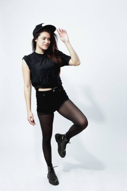 Stüdyoda beyaz zemin üzerine siyah bir tişört, şort, tayt ve kap giymiş şık siyah saçlı kız poz