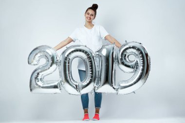 Beyaz t-shirt, kot pantolon ve numaraları 2019 stüdyoda beyaz zemin üzerine şeklinde balonlar tutan pembe çorap giymiş genç kız gülümseyerek