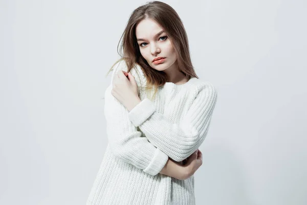 Beautiful long-haired girl in a white knitted sweater is posing on the white background in the studio — Stock Photo, Image