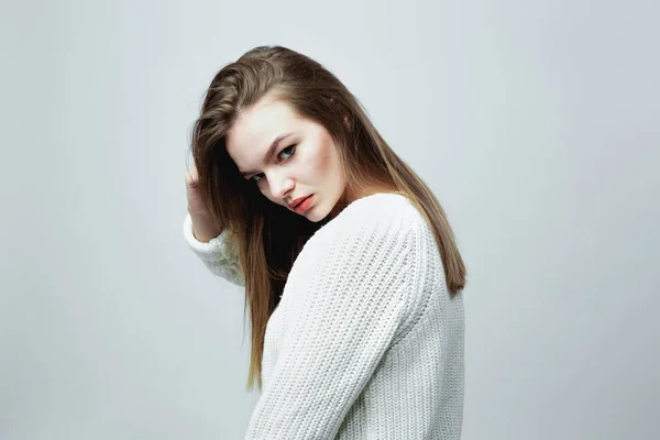 Gorgeous long-haired girl in a white knitted sweater is posing on the white background in the studio — Stock Photo, Image
