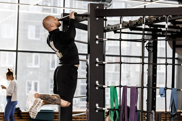 Brutaler, athletischer Mann in schwarzer Kleidung zieht an der Bar im Fitnessstudio hoch — Stockfoto