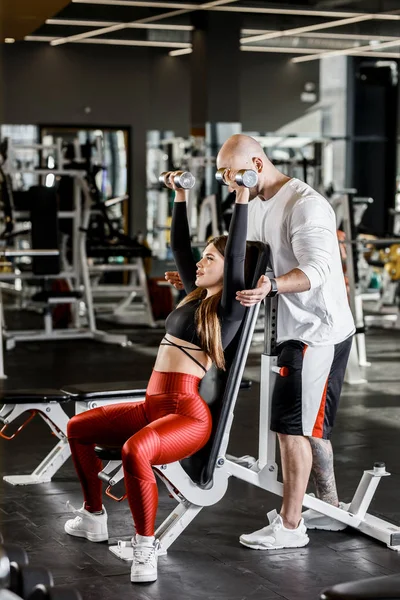 İnce güzel kız atletik adam onu modern spor salonunda sigortalanır süre kadar bir bankta oturan bir halter bench basın mı