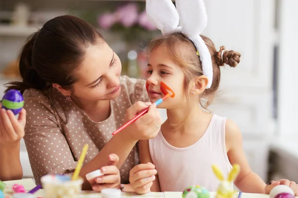 Anya lánya arc felhívja a míg a tojás a húsvét tábla a hangulatos világos konyha festése. — Stock Fotó