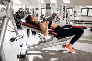 Kasları spor arabasıyla gözetimi altında dumbbells ile siyah spor top ve tayt giymiş güzel atletik kız kurar