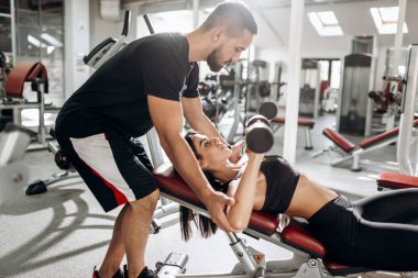 Kasları spor arabasıyla gözetimi altında dumbbells ile siyah spor top ve tayt giymiş güzel atletik kız kurar