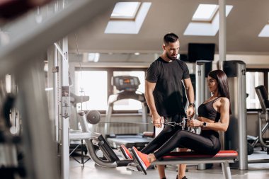 Siyah spor kıyafetlerini giymiş güzel ince kız spor salonunda antrenör gözetiminde özel egzersiz makinede karın için egzersizler yapıyor