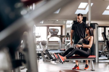 Siyah spor kıyafetlerini giymiş güzel ince kız spor salonunda antrenör gözetiminde özel egzersiz makinede karın için egzersizler yapıyor