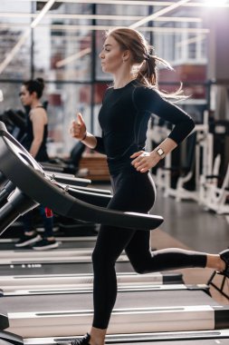 Modern spor salonunda koşu bandı üzerinde çalışan bir siyah spor giyim giymiş atletik kız