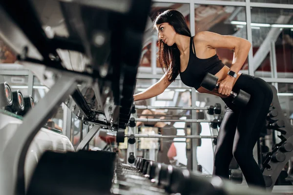 Štíhlá dívka oblečená v černé sportovní oblečení dělá triceps cvičení s činka v posilovně — Stock fotografie