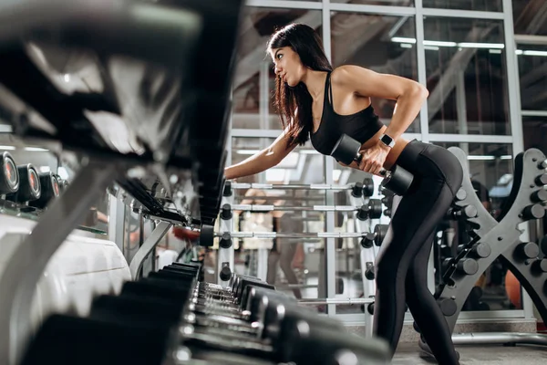 Štíhlá dívka oblečená v černé sportovní oblečení dělá triceps cvičení s činka v posilovně — Stock fotografie