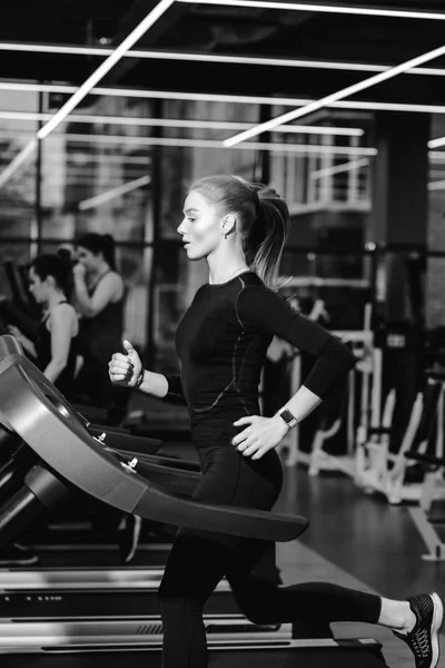 Modern spor salonunda koşu bandı üzerinde çalışan bir siyah spor giyim giymiş atletik kızın fotoğrafı siyah-beyaz — Stok fotoğraf