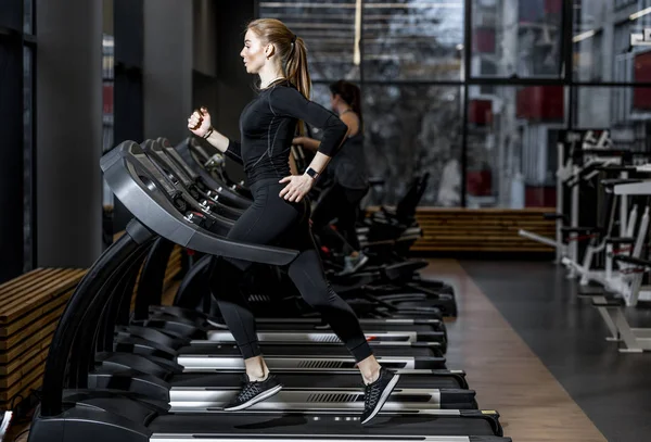 The athletic girl dressed in a black sportswear running on the treadmill in the modern gym