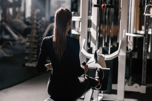 Красивая атлетическая девушка, одетая в черную спортивную одежду делает спортивные упражнения с оборудованием на скамейке в современном тренажерном зале — стоковое фото