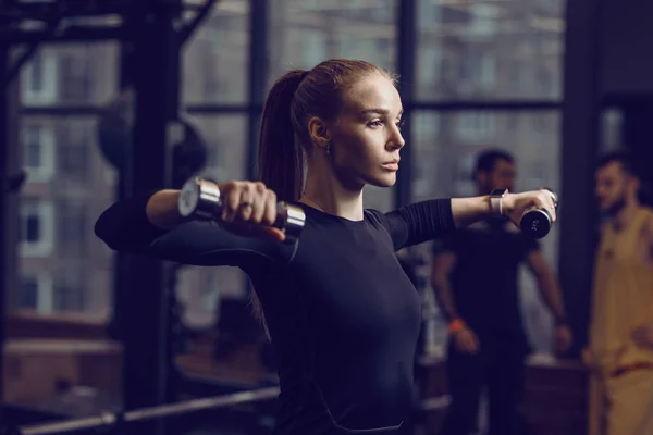 Siyah bir spor giyinen ince genç kız modern spor salonu ile lots-in Spor donatımı dumbbells ile egzersizleri yapıyor — Stok fotoğraf