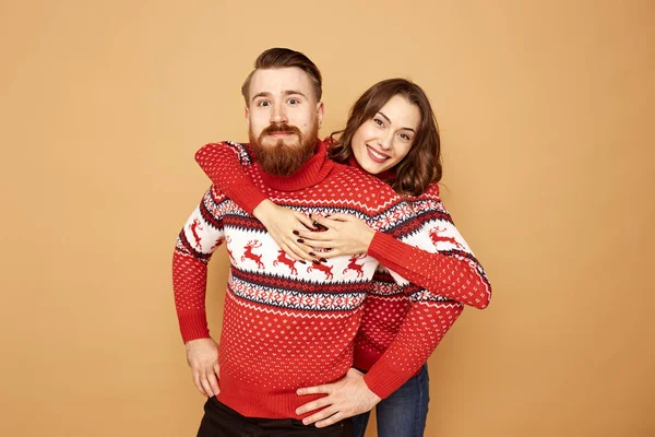 Ευτυχισμένος κορίτσι και ένας άντρας ντυμένος με κόκκινο και άσπρο πουλόβερ με τα ελάφια είναι το αγκάλιασμα σε μπεζ φόντο στο στούντιο — Φωτογραφία Αρχείου