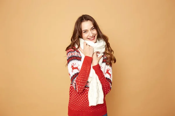 Hermosa chica vestida con un suéter rojo y blanco con ciervos y bufanda de punto blanco se encuentra en un fondo beige en el estudio — Foto de Stock