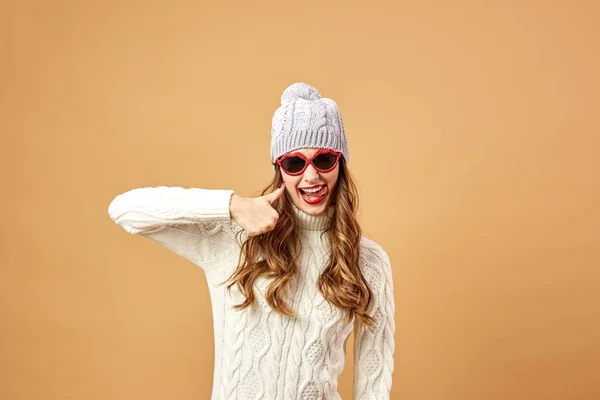 Zabawna dziewczyna ubrana w biały sweter z dzianiny i kapelusz i okulary haves zabawa na beżowym tle w studio — Zdjęcie stockowe